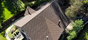 A peaked roof cricket directs rain and melting snow around a masonry chimney on a shingled roof.